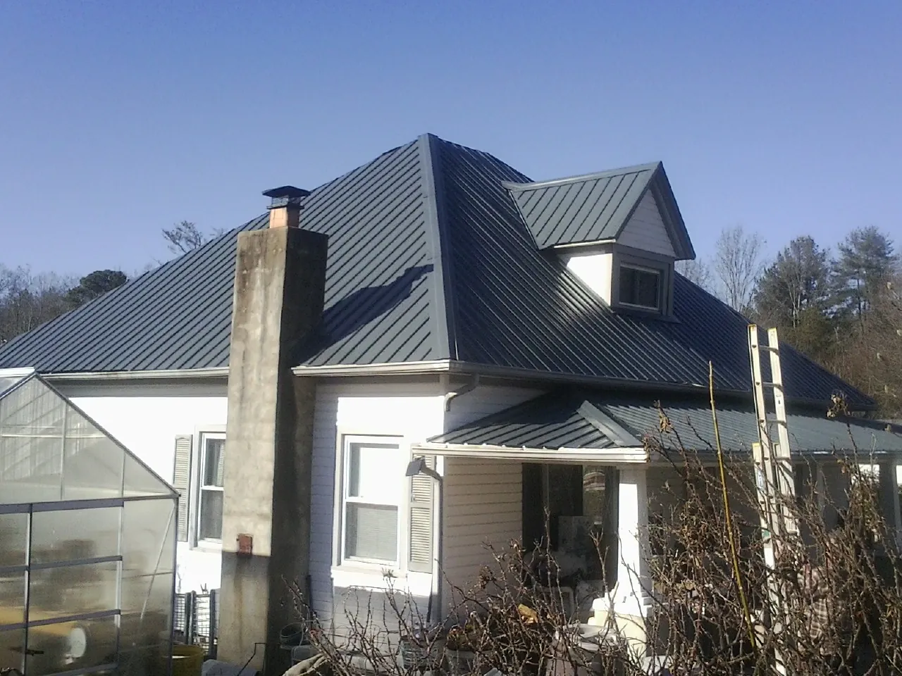 Dark blue standing seam metal roof on a white farmhouse with dormer — Slate & Tile Roof Repair by Roofing Brothers in Macy