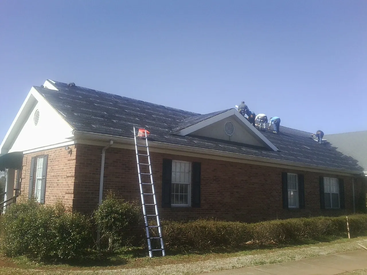 Crew tearing shingles off a brick ranch roof with a ladder set — Metal Roof Repair work by our crew in Macy