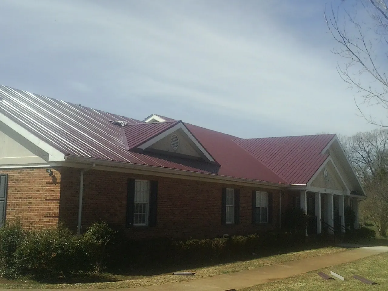 Red metal roof with gabled entries on a long brick building, from a Hail Damage Roof Repair job in Macy
