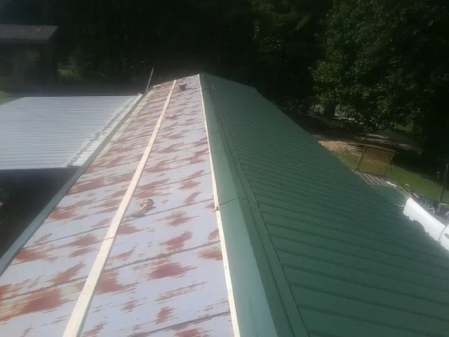 Old rusted panels beside newly installed green metal roofing — Wind Damage Roof Repair by Roofing Brothers in Macy