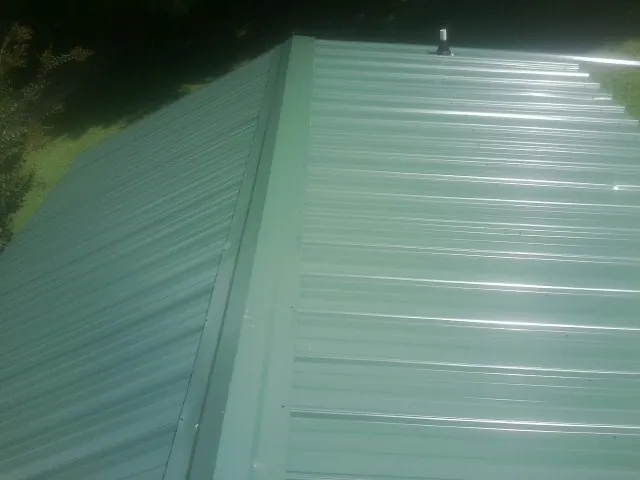 New green metal panels meeting at the ridge of a roof — Flat Roof Repair work by our crew in Macy