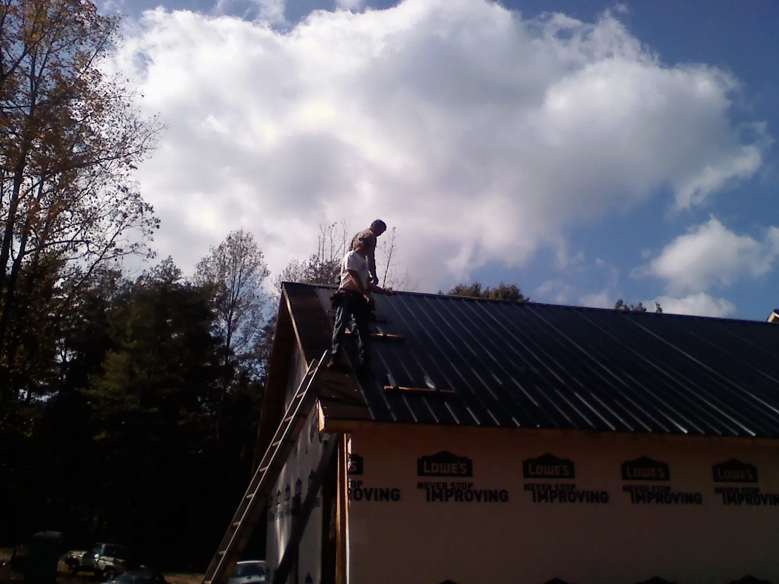 Roofer fastening dark metal panels high against a cloudy sky, from a Roof Inspection job in Macy